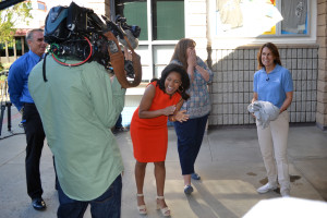 A Helpful Honda team member (right) removes her sweater to reveal her identity. Beth Holen (center) reacts as Sheinelle Jones of the TODAY show (left) watches.