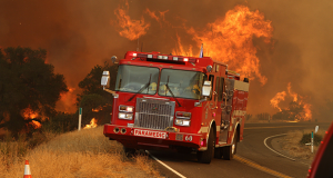 A fire engine parked in front of an active blaze.