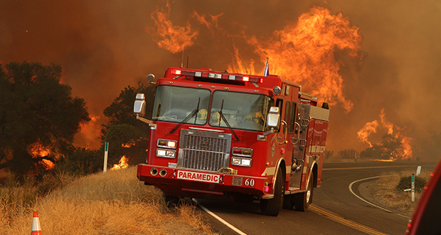 A fire engine parked in front of an active blaze.