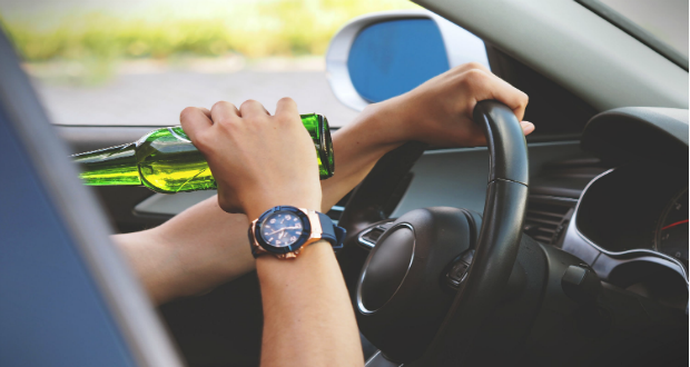 A person driving while drinking from an unlabeled glass bottle.