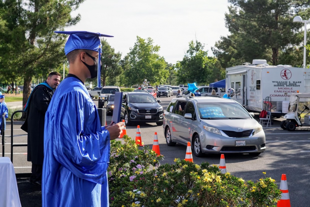 A student holding their diploma as a decorated vehicle passes.