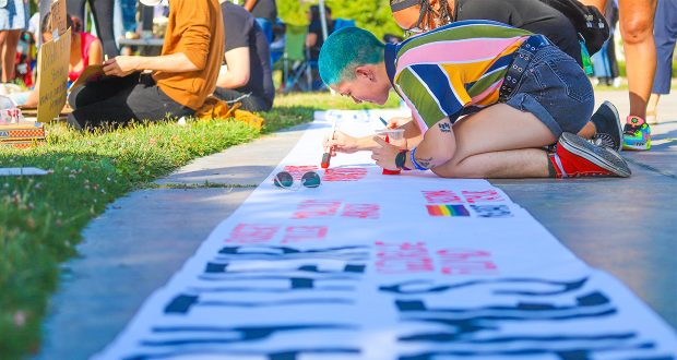Girl painting name of African American life lost to police on banner in park.