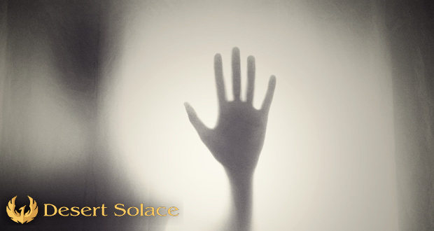 Desert Solace - Inpatient Addiction Treatment Center Explains How Trauma Affects Addiction - A silhouette of a person with their hand outstretched behind frosted glass