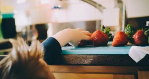 Kid reaching for strawberries in kitchen