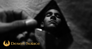 Desert Solace - Desert Solace Co-Founder Explains Role Of Self-Acceptance In Addiction Treatment - A black and white photo of a man holding a mirror shard, his neutral face reflected inside.