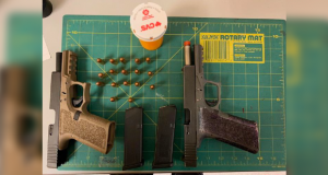 Two handguns, 17 rounds, and a CVS pill bottle lay on a green mat with measurments on it to display their sizes.