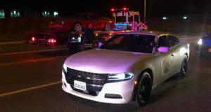 A red car loaded onto a tow truck, with a CHP cruiser next to it.