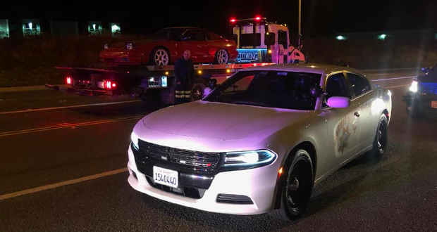 A red car loaded onto a tow truck, with a CHP cruiser next to it.