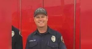 Photo of Tory Carlon, a firefighter in uniform stands in front of an engine