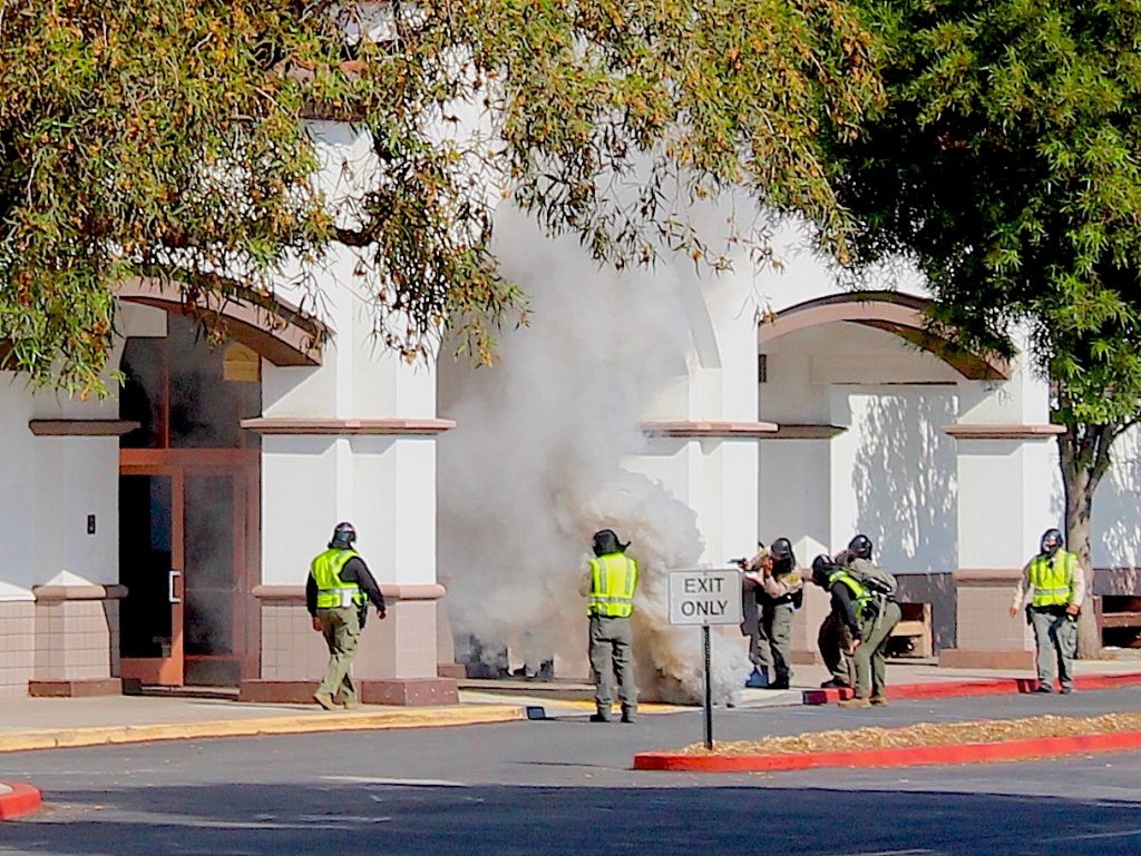 Deputies stand outside the old Sears building with guns drawn in front of a cloud of smoke